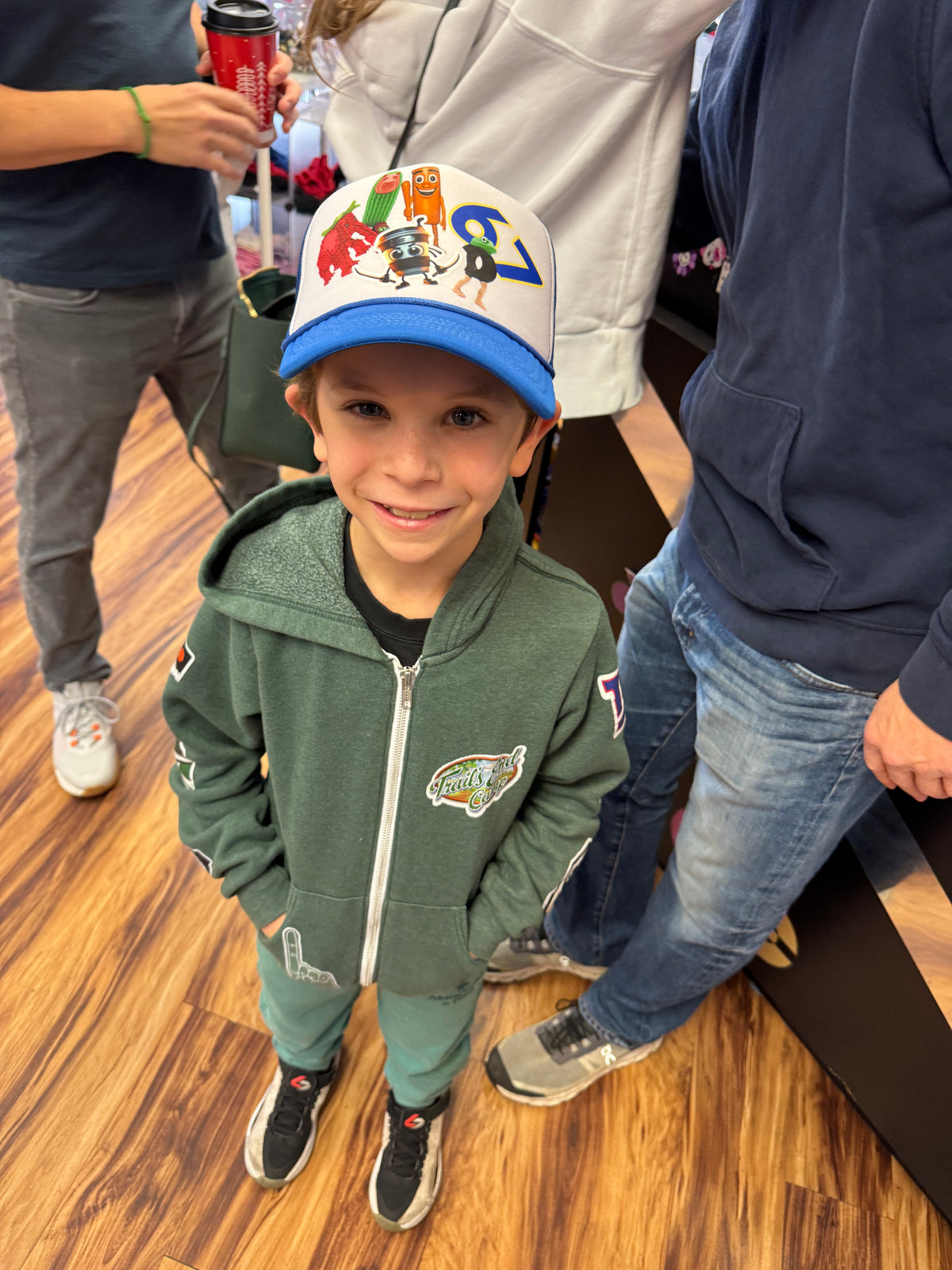 Smiling boy wearing a blue and white custom trucker hat with patches and a green zip hoodie