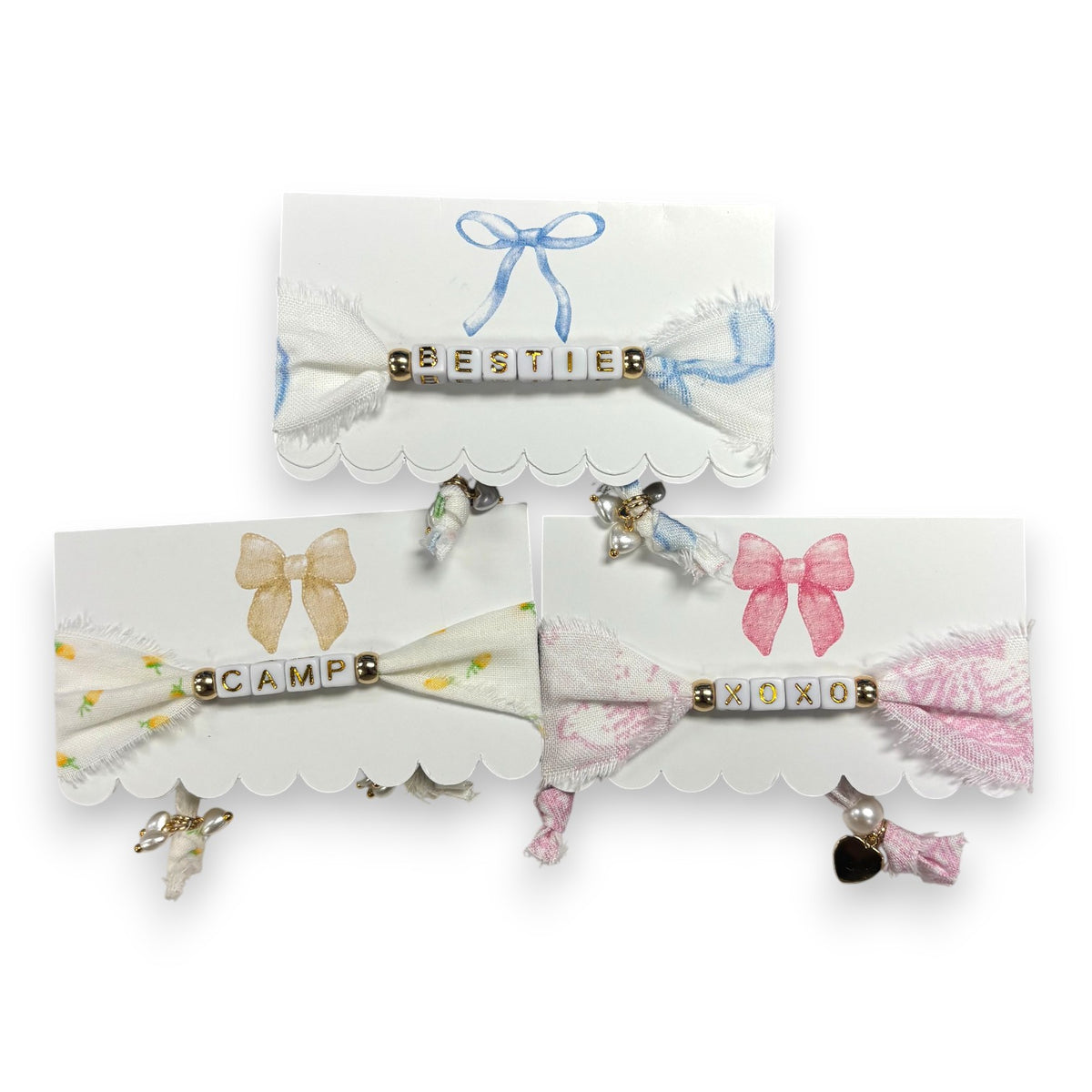 Three coquette beaded bracelets spelling BESTIE, CAMP and XOXO on frayed floral fabric with watercolor bows
