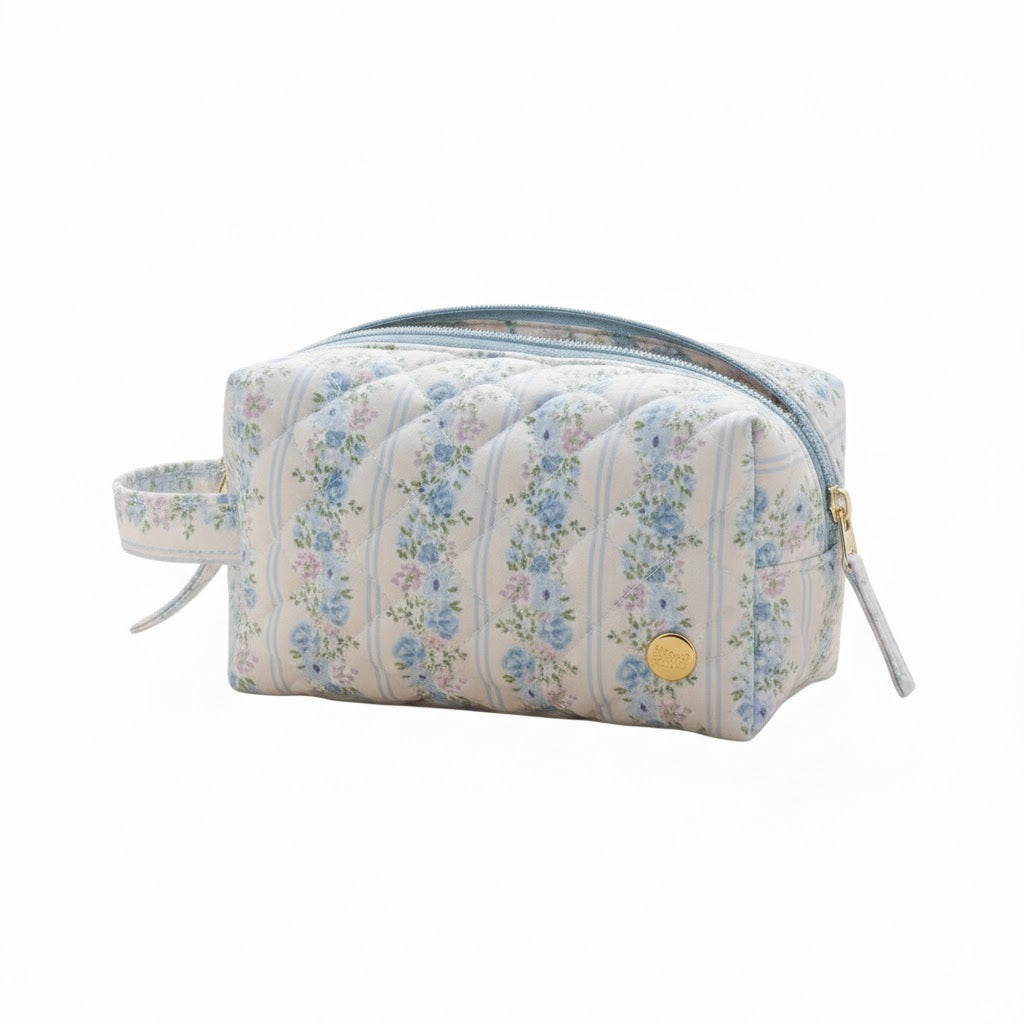 Blue floral striped quilted cosmetic pouch with a gold snap logo and zipper, side angle