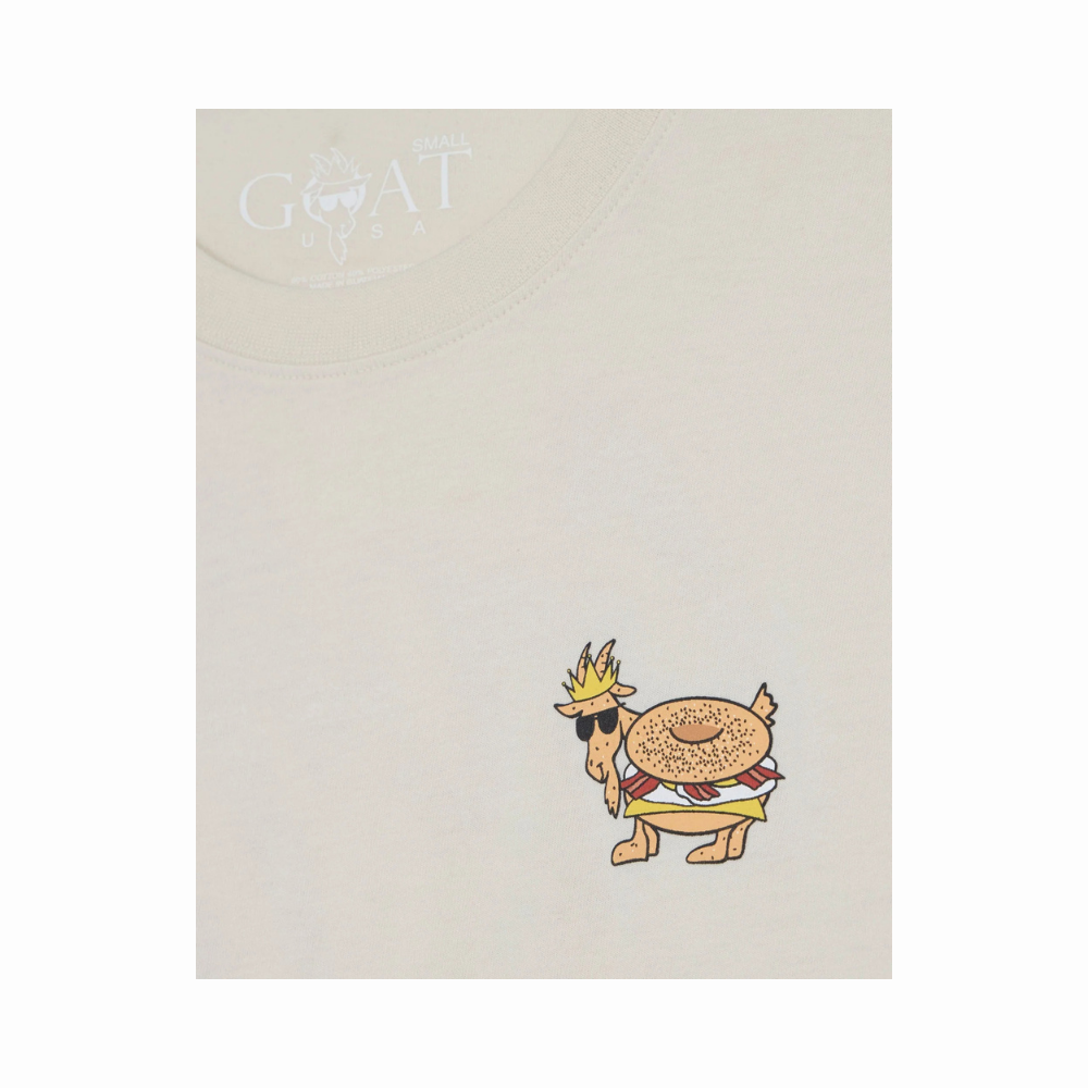 GOAT Breakfast T-Shirt front chest detail showing small embroidered goat-bagel character logo on cream cotton shirt