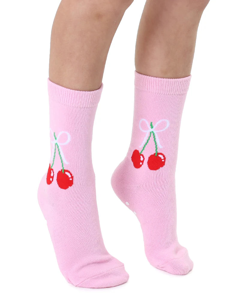 Child's legs wearing pink crew socks with red cherries and a white bow