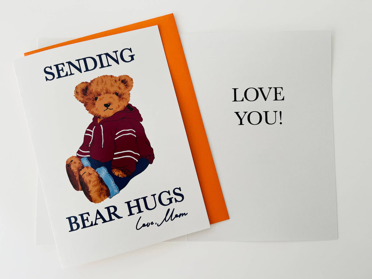 Sending Bear Hugs Love Mom card with teddy bear in maroon striped hoodie and jeans, shown with orange envelope on gray background