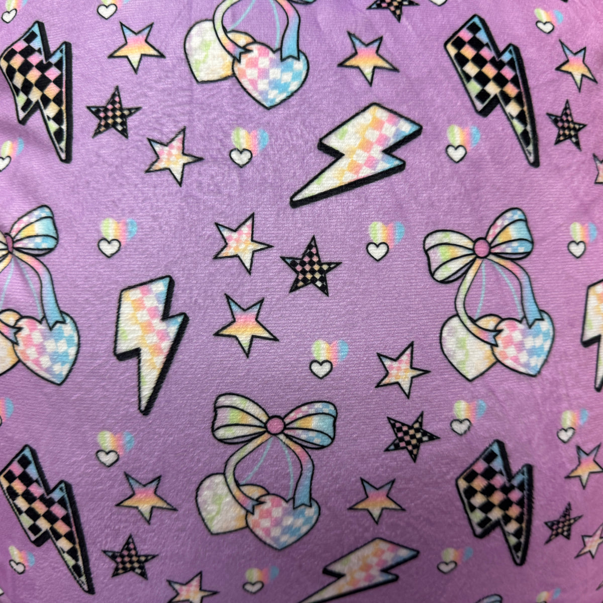 Electric Cherries Camp Boyfriend Pillow fabric close-up of checkered bows, hearts and bolts on purple