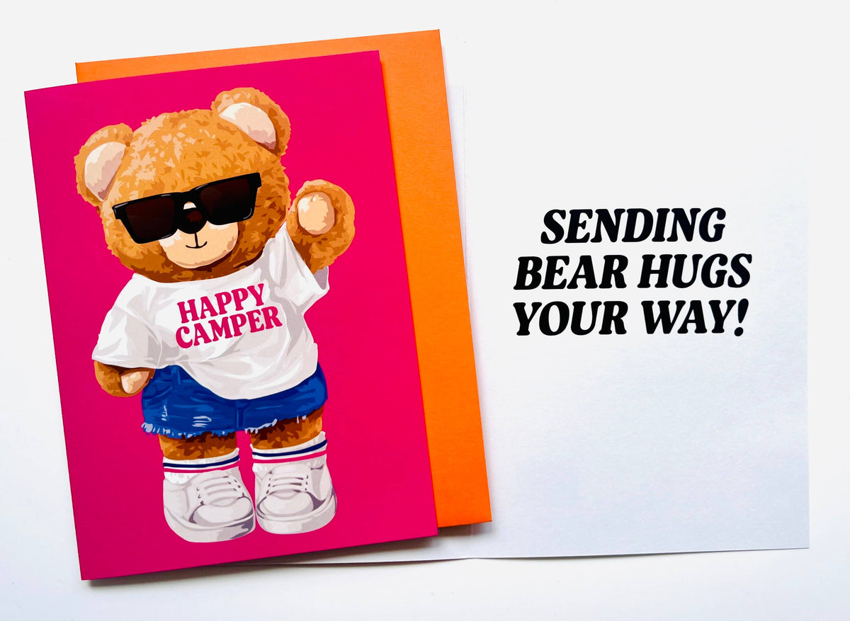 Happy Camper teddy bear greeting card with bear wearing sunglasses and white tee on hot pink background, shown with orange envelope and white card displaying Sending bear hugs your way message
