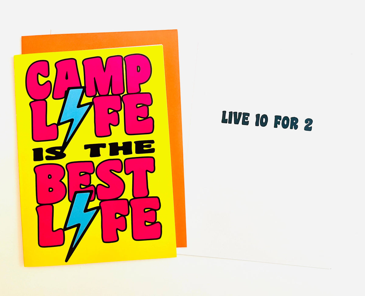 Camp Life is the Best Life greeting card with hot pink bold letters and blue lightning bolts on bright yellow background, shown with orange envelope behind it
