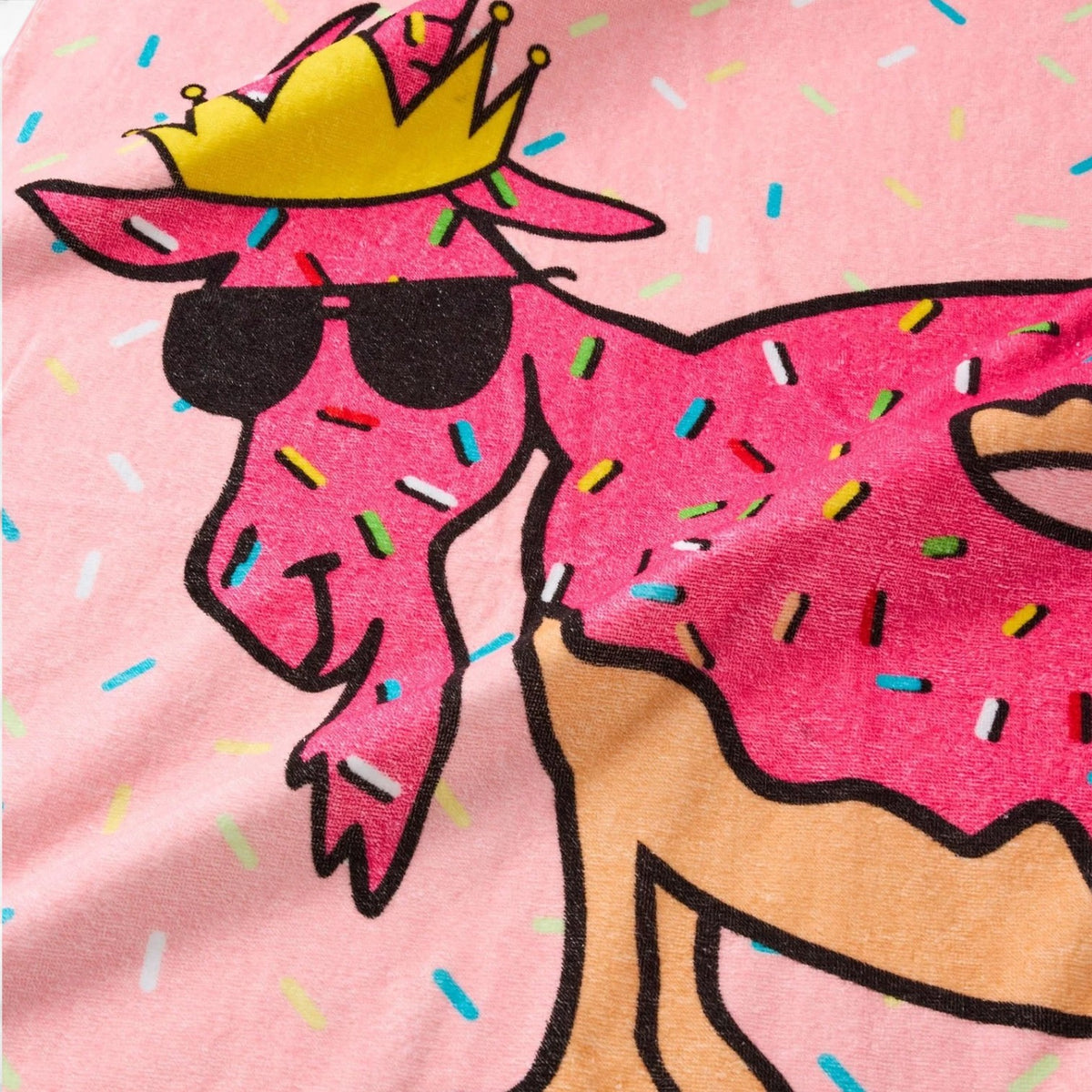 Close up detail of Donut Beach GOAT towel showing pink llama with donut body texture wearing crown and sunglasses with rainbow sprinkles on pink background